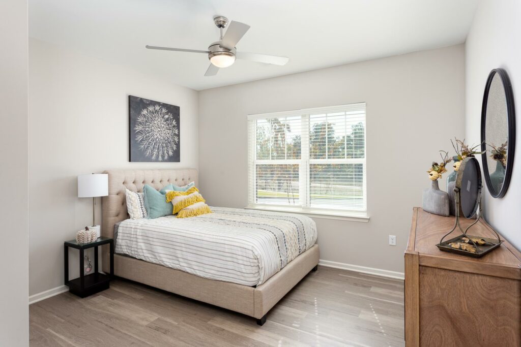 Model bedroom with large bed, ceiling fan, dresser, and large window at Moonlight Apartments in Austin, TX